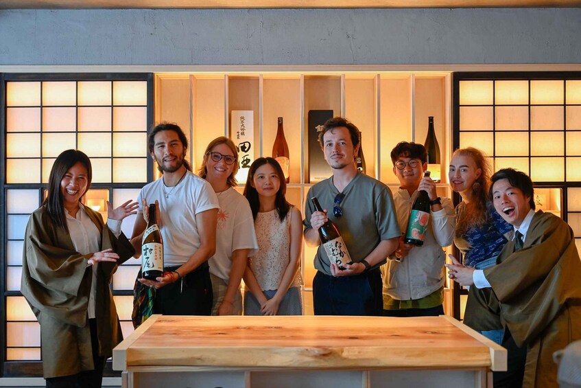 A group of people standing in front of a wooden table with bottles of wine. 2