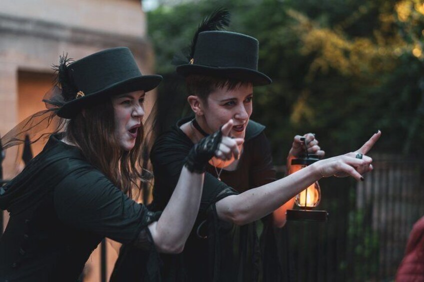 Two people in black attire with feathered hats, one holding a lantern. 4