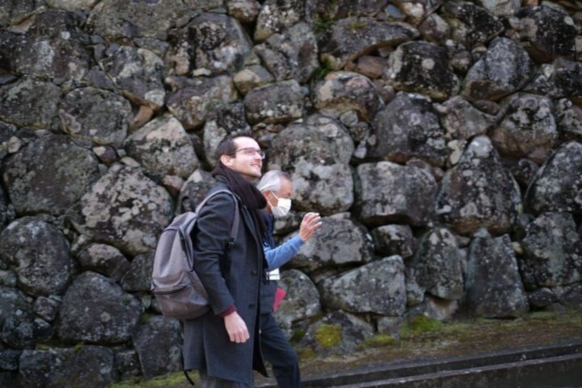 Two people walking past a stone wall. 2