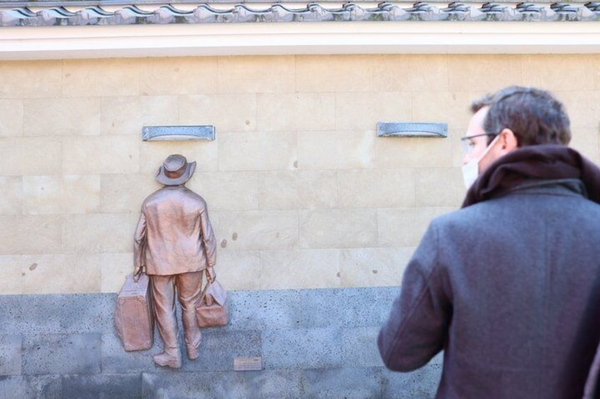 A bronze statue of a man with a hat and briefcase on a wall. 5