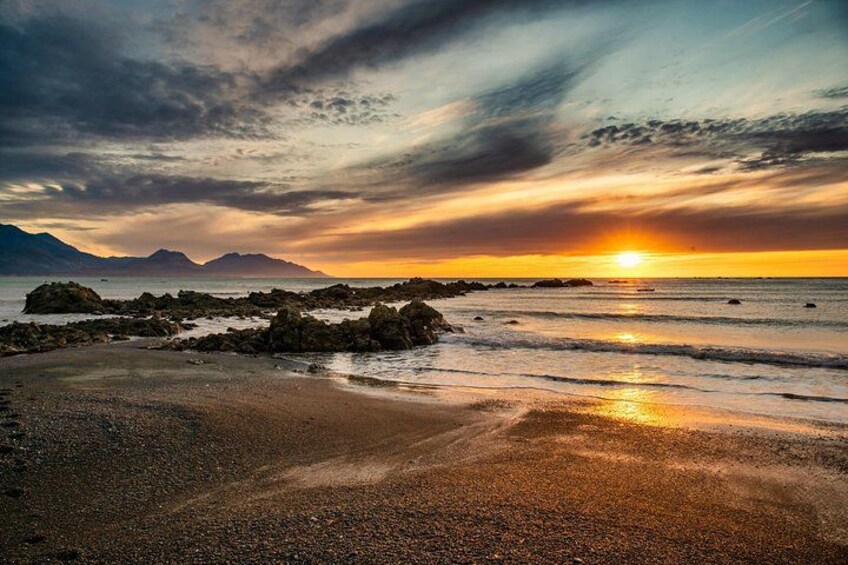A beach with rocks, a sunset, and mountains in the background. 4