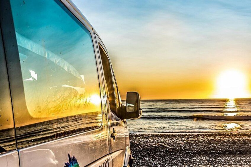 A vehicle parked on a beach with the sun setting in the background. 1