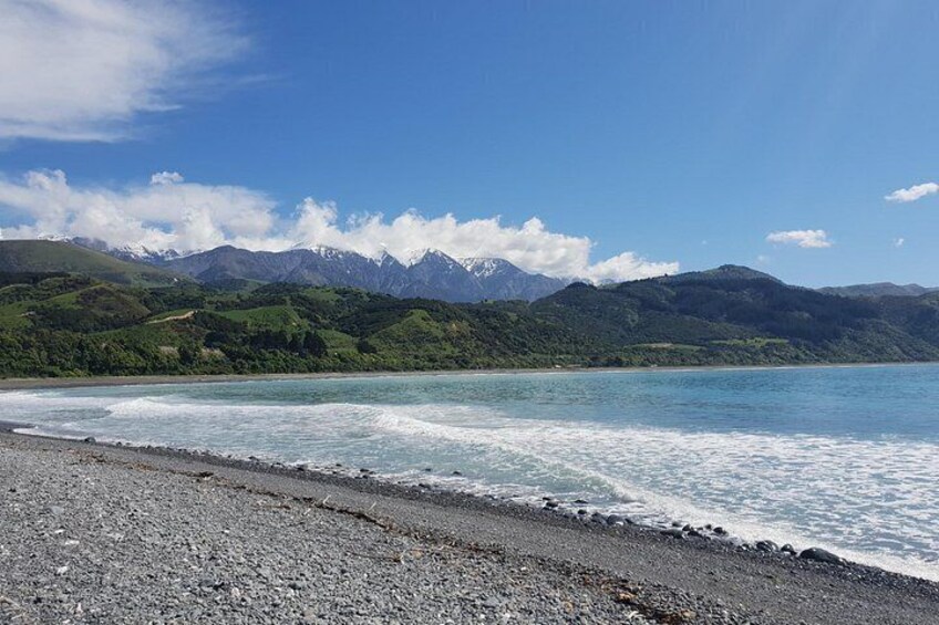 A beach with a rocky shoreline, calm water, and mountains in the background. 3