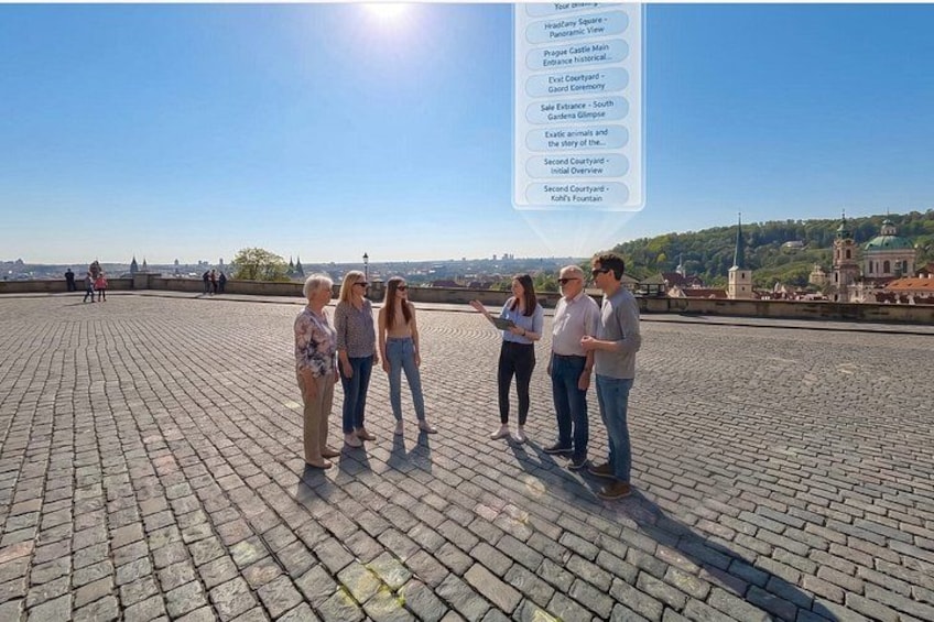 A group of people standing on a paved area with a clear view of a castle and surrounding landscape. 3