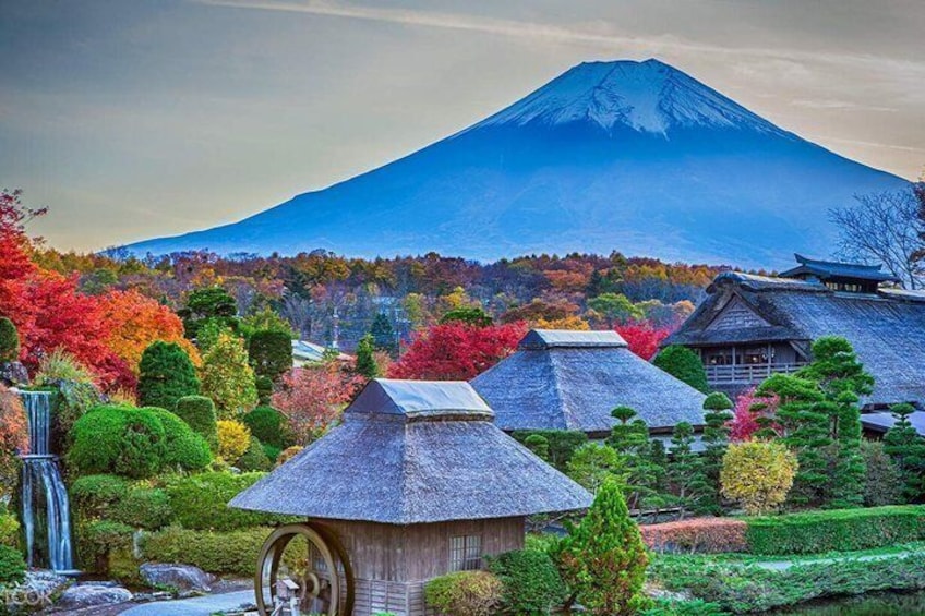 A traditional Japanese village with thatched-roof houses, a waterfall, and Mount Fuji in the background. 1