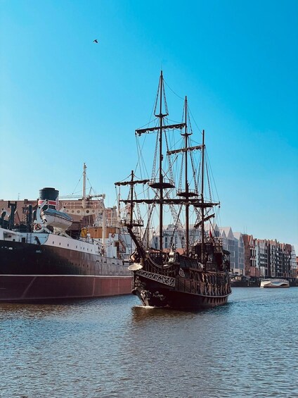 A tall ship docked at a harbor with buildings in the background. 4
