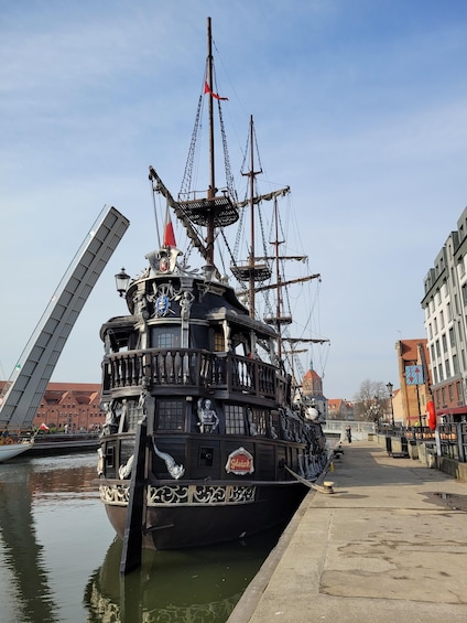A large, ornate ship docked at a pier with a bridge in the background. 2