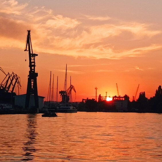 A sunset over a harbor with cranes and boats. 1