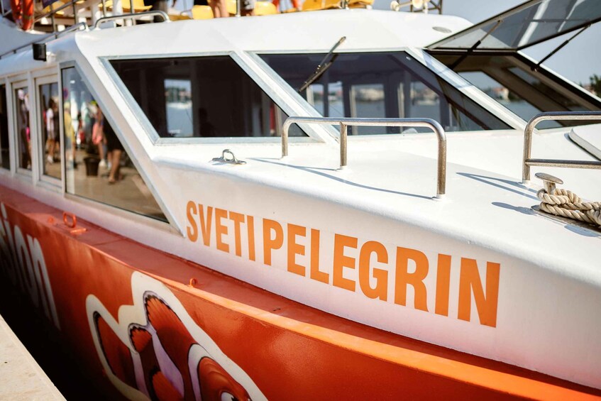 A boat named 'Sveti Pelegrin' with a white and orange color scheme, metal railings, and a rope tied to the side. 2