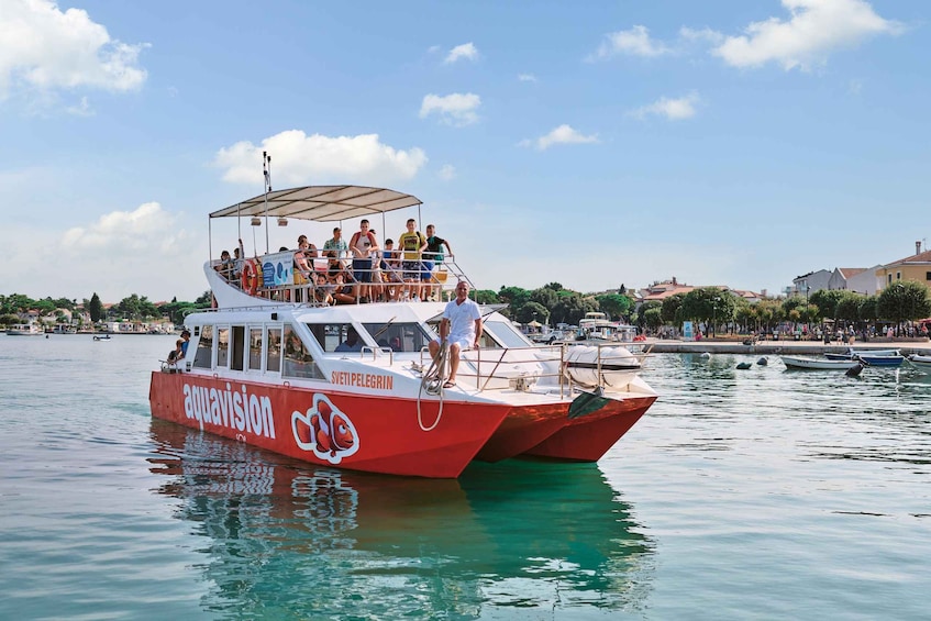 A red boat with 'aquavision' written on it, docked at a marina with people on board. 1