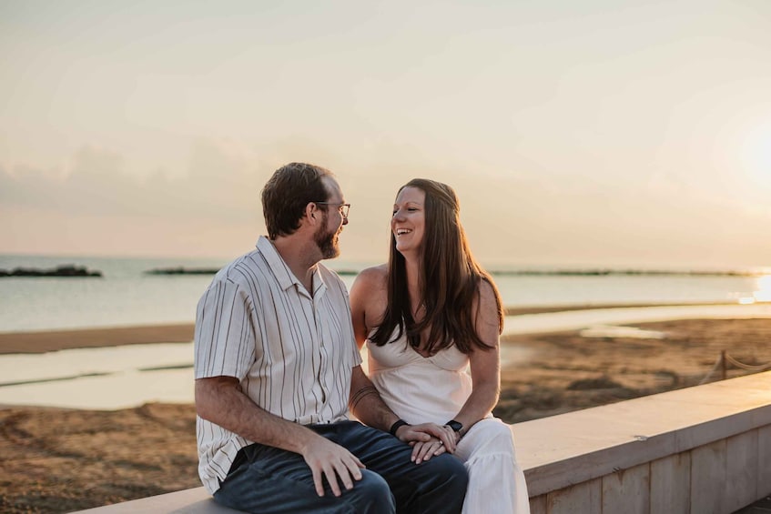 A couple sitting on a concrete ledge overlooking a beach with a calm sea and a sunset in the background. 5