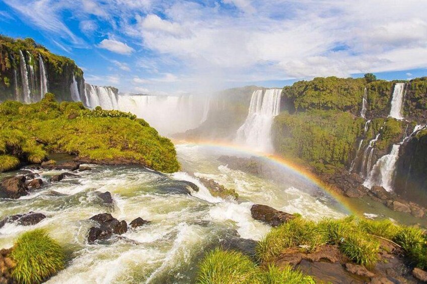 Una cascada con un arcoíris, abundante vegetación y un río. 5