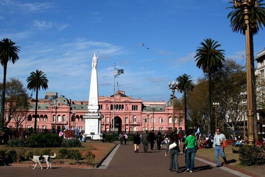Una plaza pública con un edificio rosa, un monumento blanco y palmeras. 2