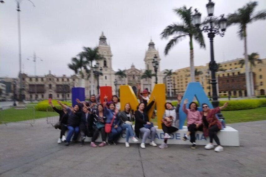 A group of people posing in front of large colorful letters spelling 'MALAGA' with a historic building in the background. 1