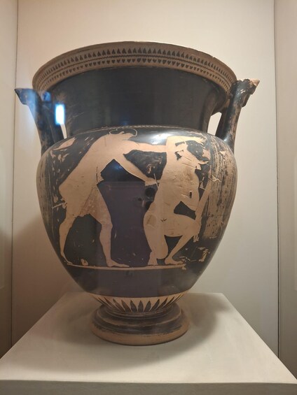 An ancient Greek vase with black and red painted figures, displayed on a pedestal. 4