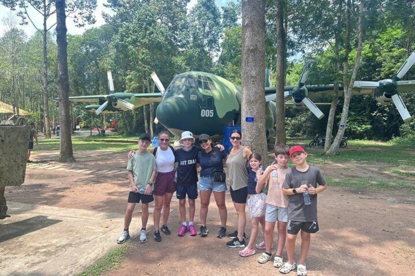 A group of people standing in front of a green military aircraft with the number 005. 1