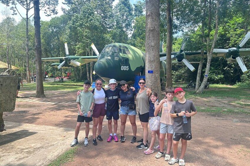 A group of people standing in front of a green military aircraft with the number 005. 1