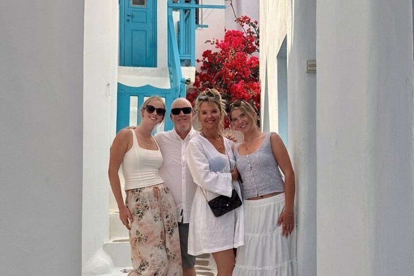Une rue étroite bordée de bâtiments blancs aux portes bleues, et entourée de fleurs rouges. 1