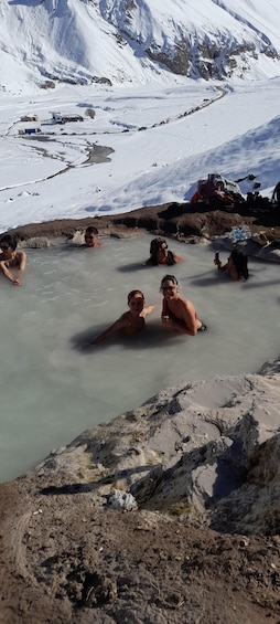 A group of people in a geothermal hot spring surrounded by snow-covered mountains. 1