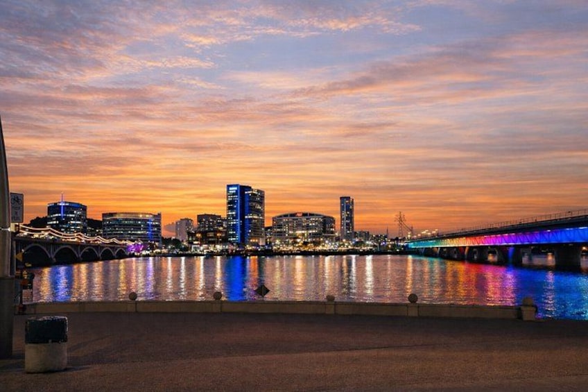 A city skyline at dusk with illuminated buildings and a bridge reflecting on the water. 1