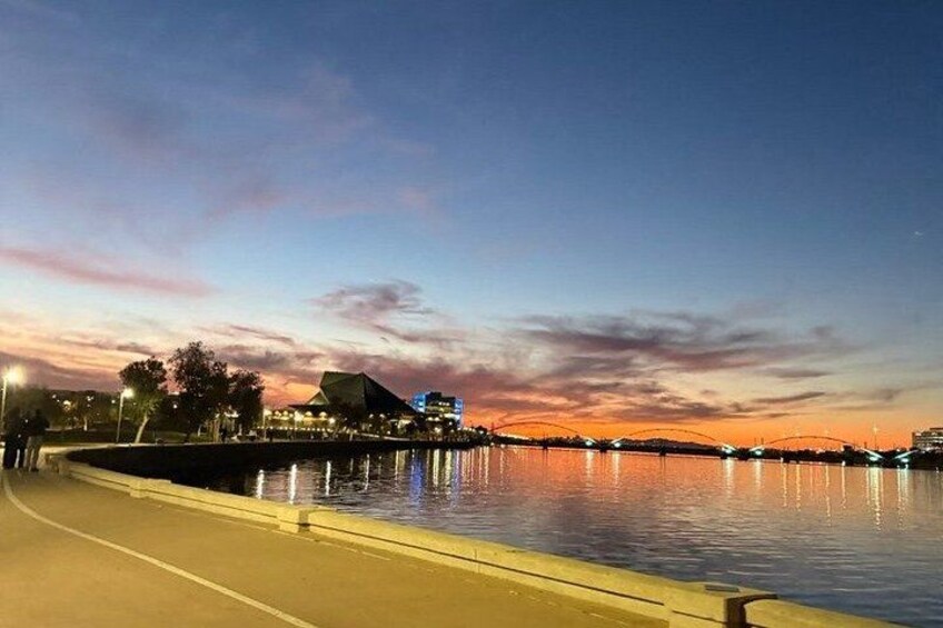 A waterfront at dusk with a bridge, buildings, and a walkway. 5