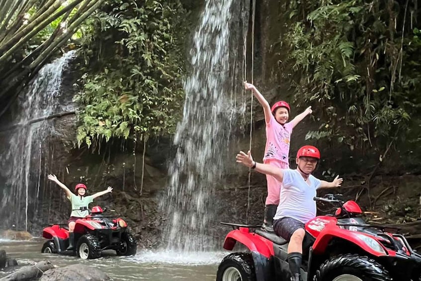 People on ATVs near a waterfall in a forested area. 3