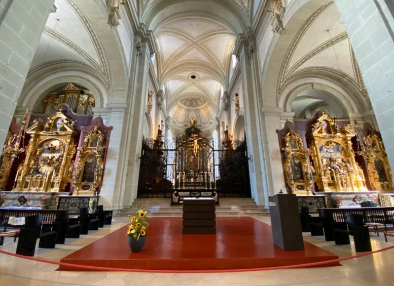 An ornate church interior with high vaulted ceilings, golden altars, and a central altar. 3