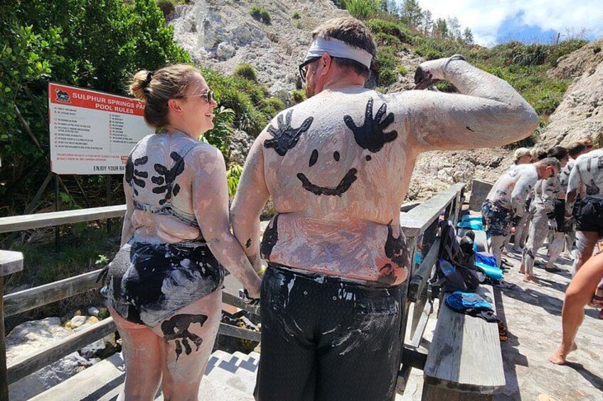 Des personnes couvertes de peinture sur une plage, avec un panneau indiquant les règles à respecter au bord des sources sulfureuses. 3