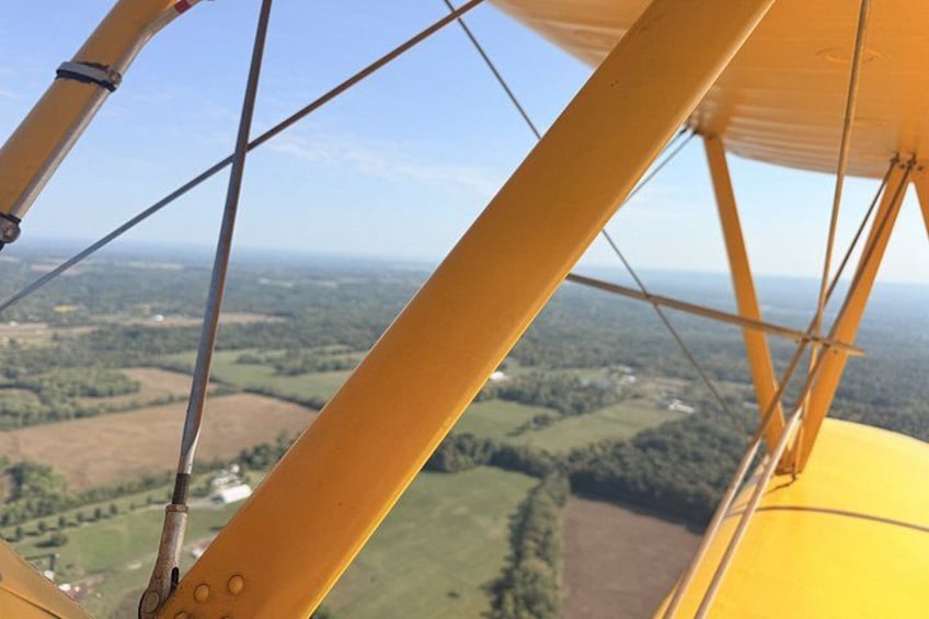 A yellow biplane with a clear view of the countryside below. 3