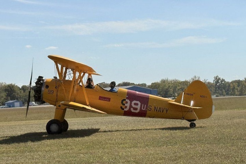 A yellow biplane with '99 U.S. Navy' markings parked on a grassy field. 3