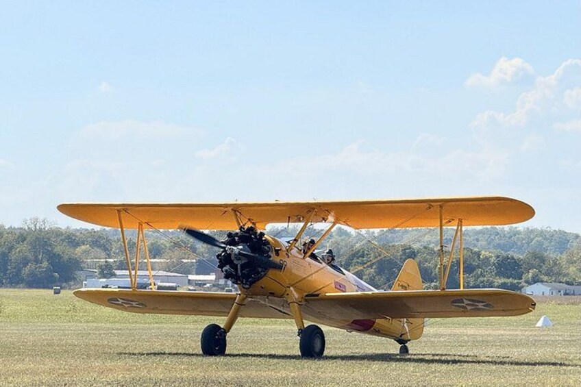 A yellow biplane on a grassy field with a clear sky and trees in the background. 4