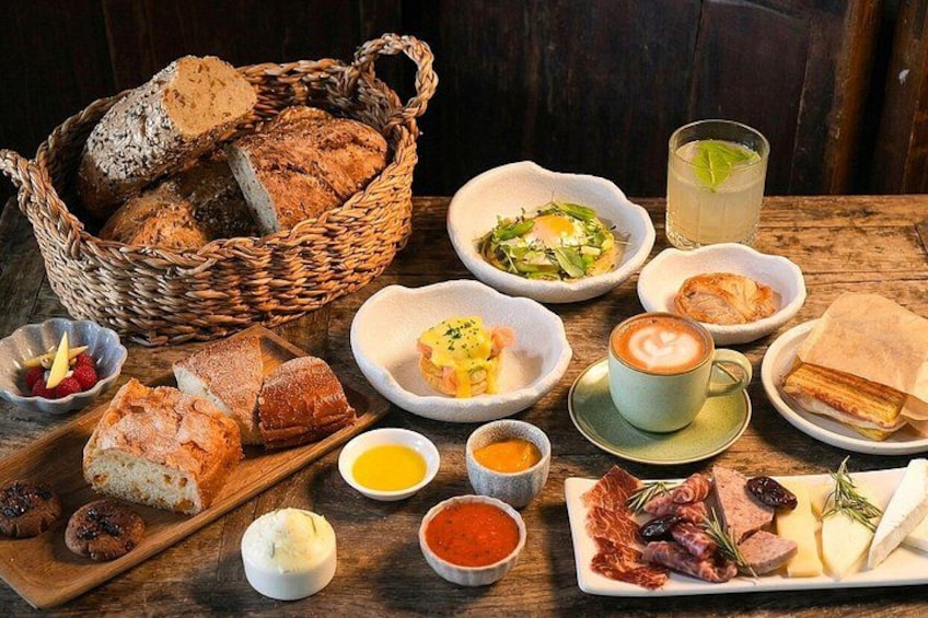 A variety of food items including bread, cheese, meats, and a cup of coffee on a wooden table. 1