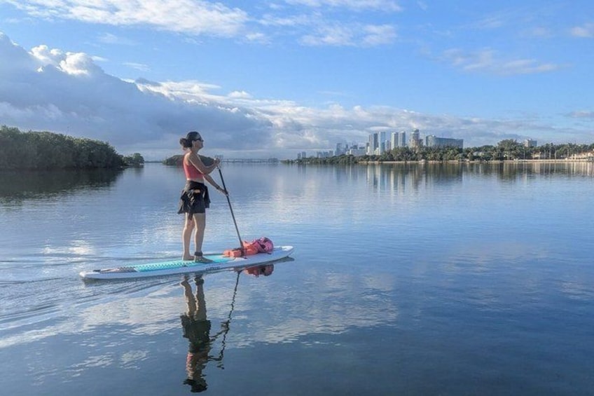 A person paddleboarding on calm water with a cityscape in the background. 2