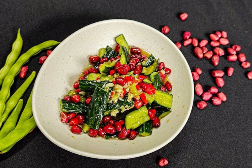 A bowl of salad with green vegetables, red pomegranate seeds, and green beans on a dark surface. 2