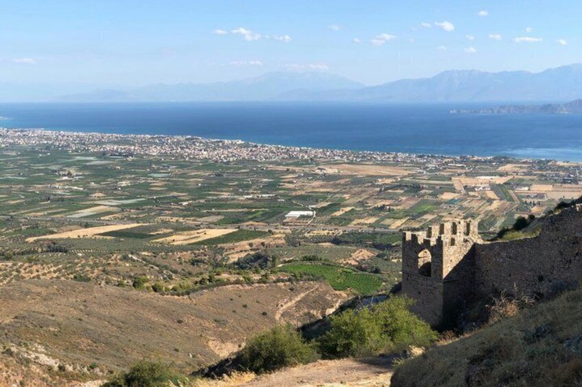 Un paisaje costero con una torre de piedra histórica, campos y una ciudad distante junto al mar. 4