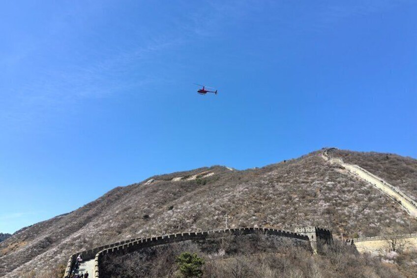 Un hélicoptère survole un paysage montagneux, avec un mur de pierres et un ciel bleu dégagé. 2