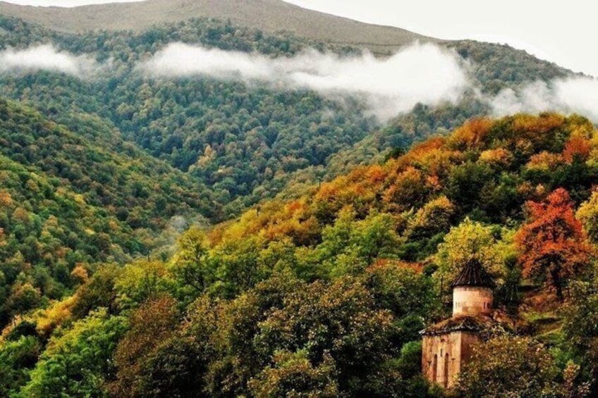 A forested mountain with autumn foliage and a small stone structure. 4