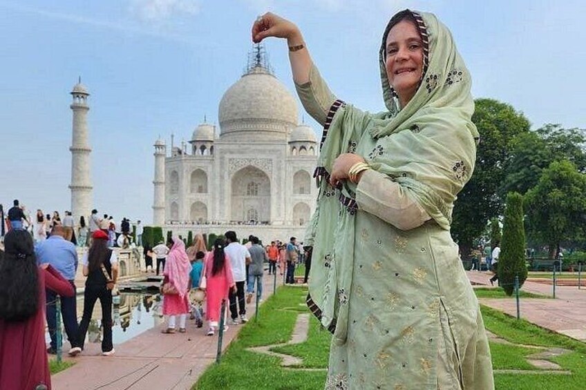 Una persona vestida con traje tradicional frente al Taj Mahal, con el monumento y una multitud de visitantes al fondo. 1
