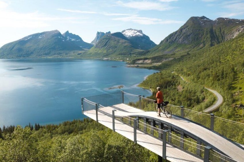 A person riding a bicycle on a bridge with a scenic view of a lake and mountains. 1