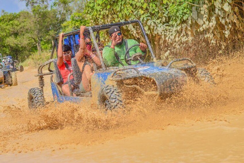 A blue off-road vehicle driving through a muddy area with passengers. 1
