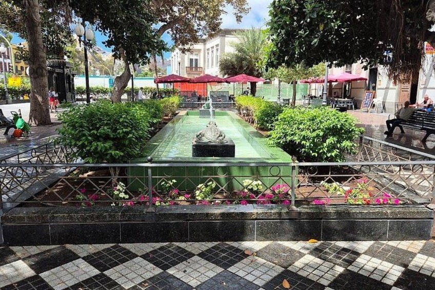 A public square with a fountain, benches, and potted plants. 1