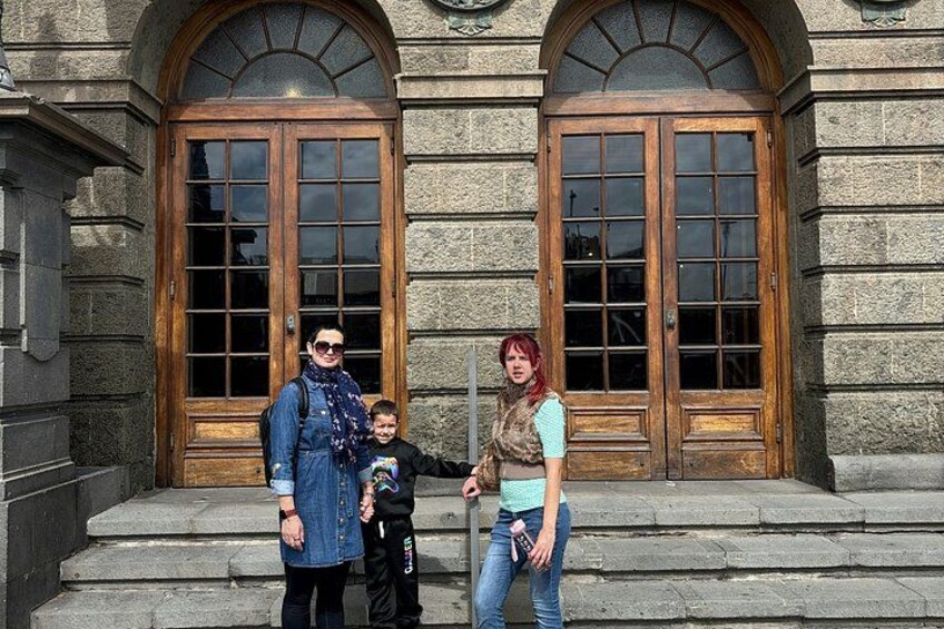 A family of three in front of a stone building with two large wooden doors. 2