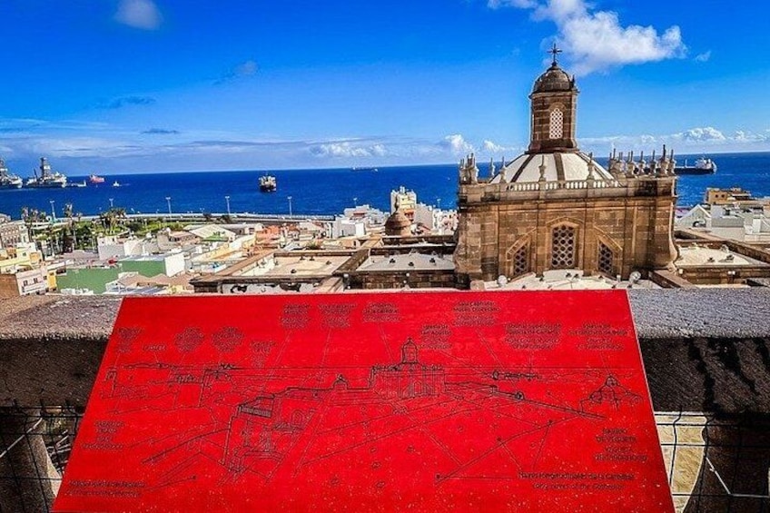A coastal cityscape with a prominent church, a red banner with text, and ships in the distance. 4