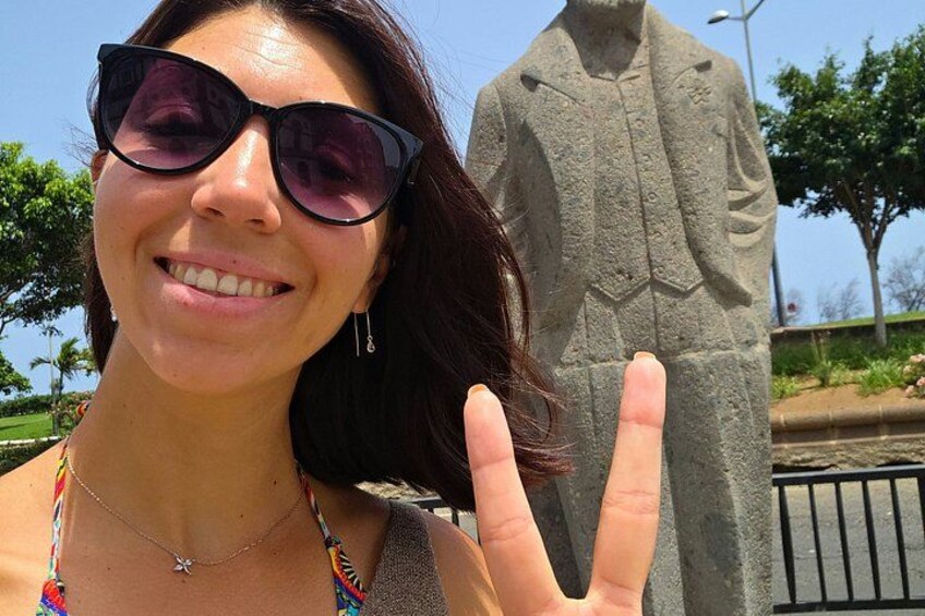A person with a peace sign, a statue, and a clear sky. 3