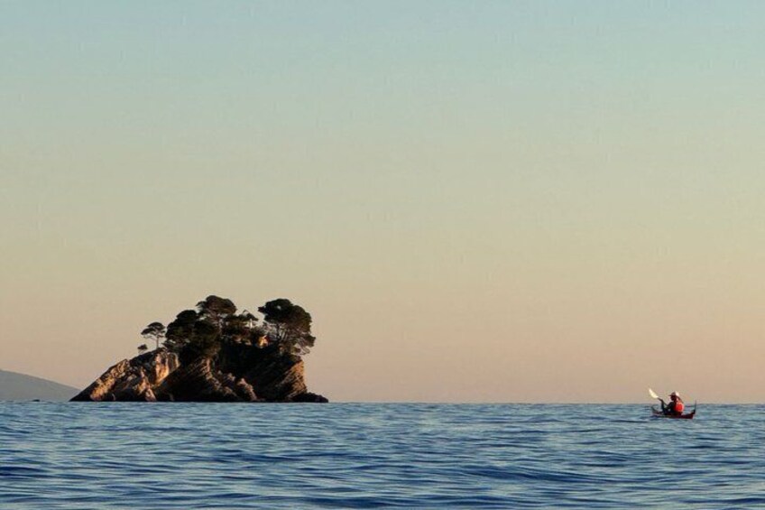 A calm sea with a rocky outcrop and a small boat with a person in the distance. 4