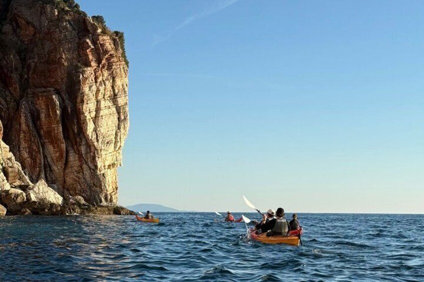 A rocky cliff by the sea with people paddling in small boats. 2