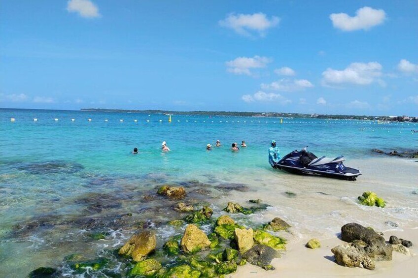 A clear beach with rocks, a jet ski, and people swimming. 3