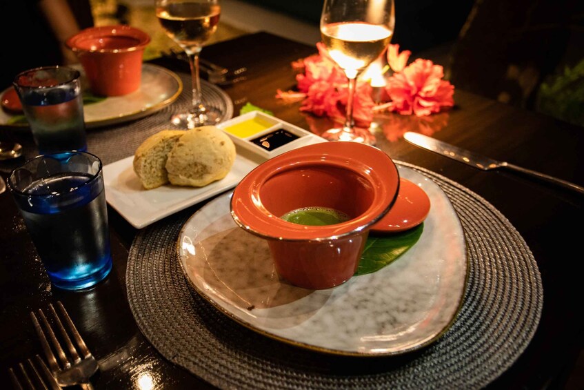 A table with a plate of food, two red bowls, a glass of water, and a lit candle. 3