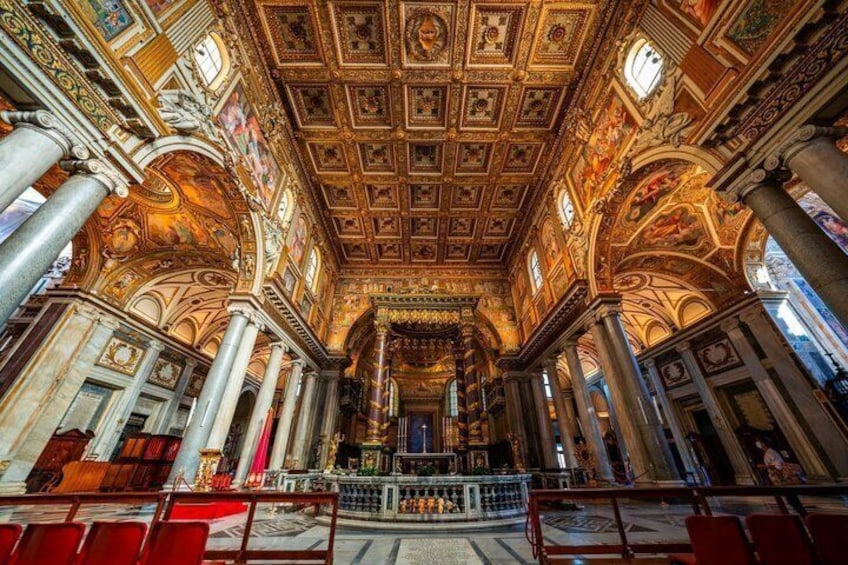 Interior ornamentado de una iglesia con frescos detallados en el techo, grandes columnas y un altar central. 2