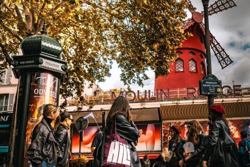 A busy street with a red building, a sign for 'Theatre,' and a crowd of people. 1